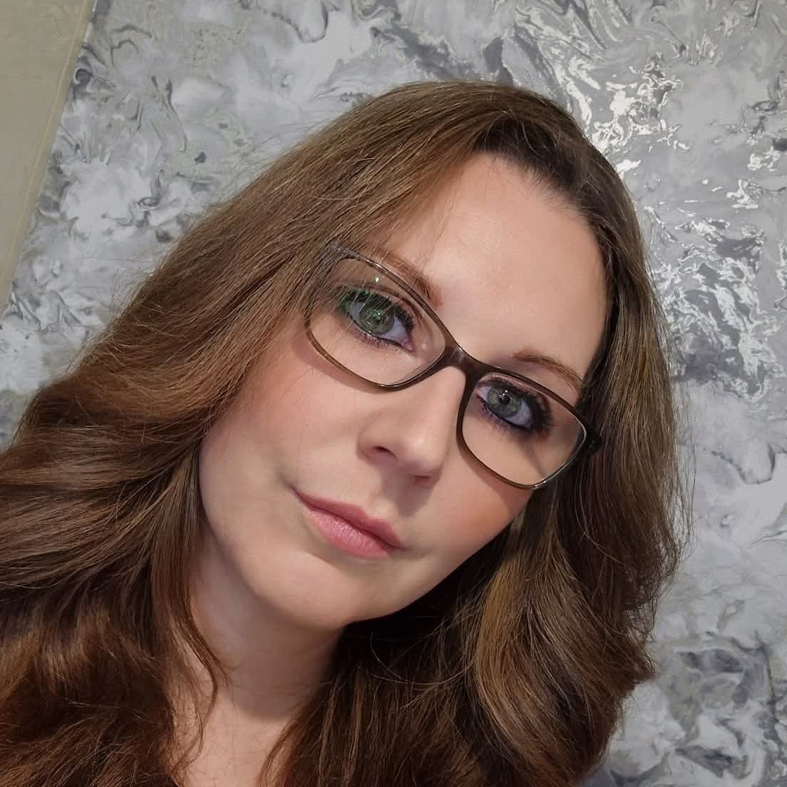 Woman wearing glasses with a marble-patterned wall in the background
creator of huglets